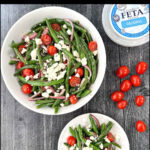 aerial bowl and plate with Greek green bean salad recipe and fresh grape tomatoes and a container of feta cheese and text