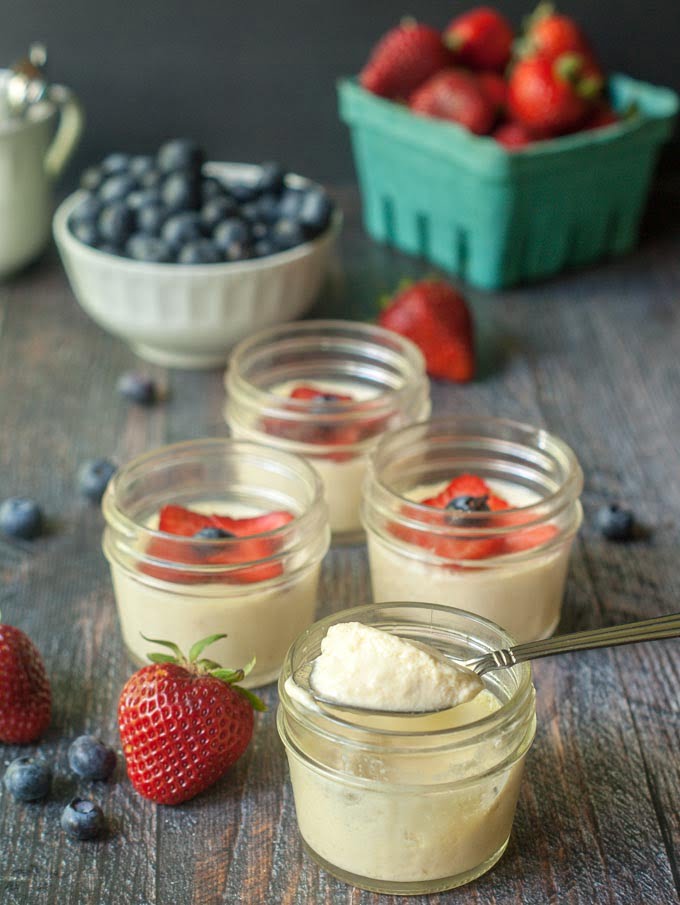 jars of mousse with a spoon dipping in and fresh berries in the background and scattered around