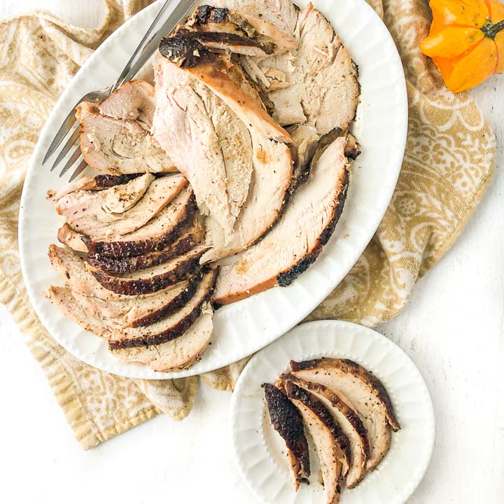 white plate and platter with brined smoked turkey breast slices and beige tea towel underneath