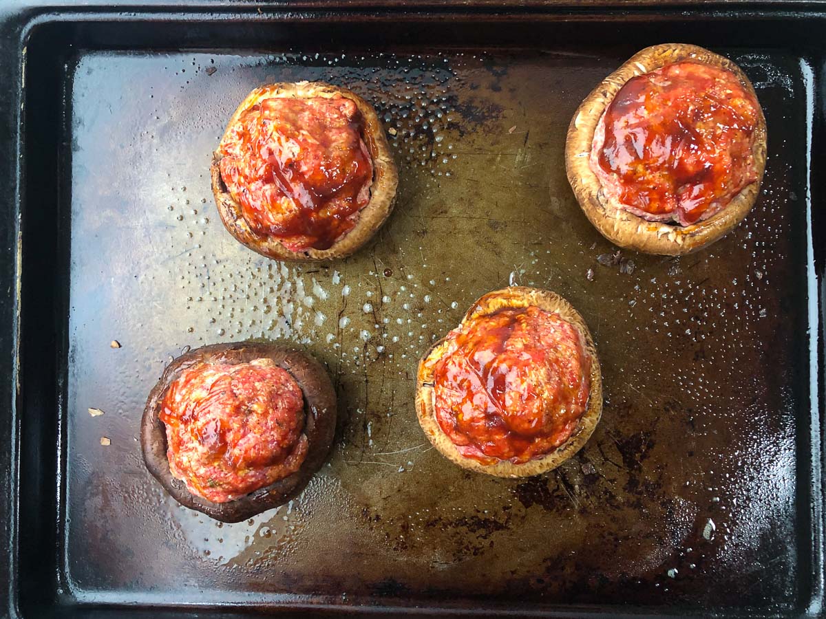baking try with 4 raw stuffed portobellos with bbq sauce on top