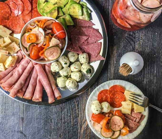 round silver relish tray with meats and cheese and a bowl and jar with pickled ratatouille vegetables.