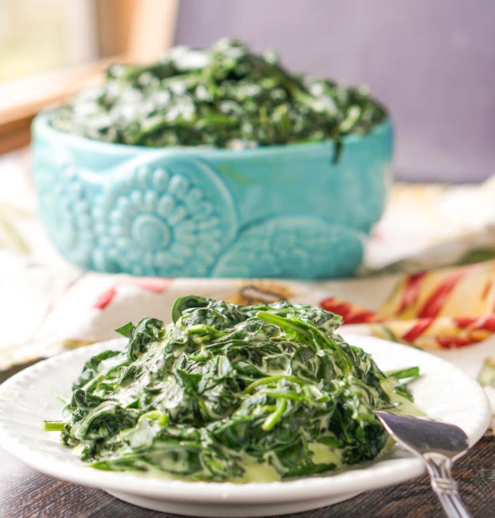 closeup of white plate with creamed spinach and blue bowl in background