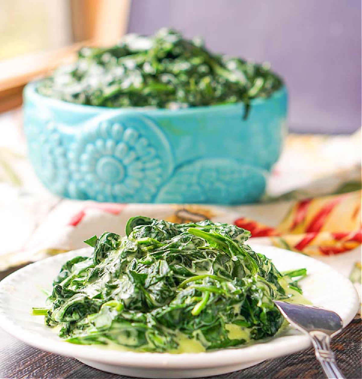 white plate with cheesy spinach and blue bowl in the background