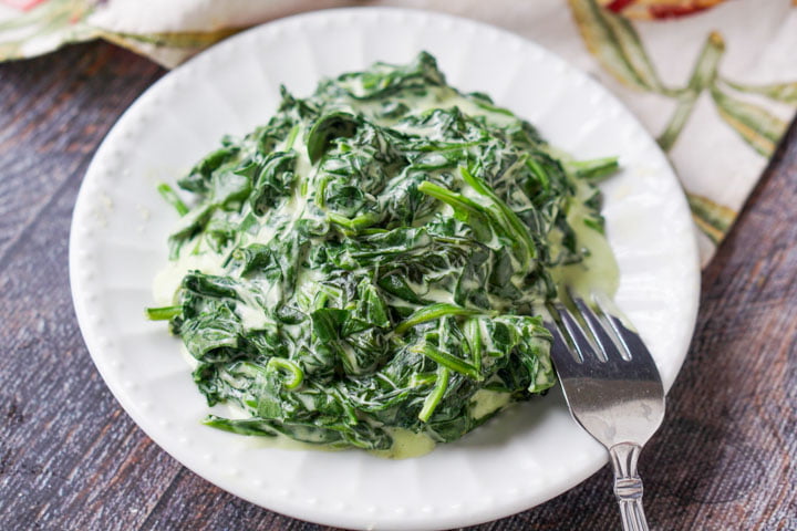 closeup of white plate of spinach side dish with a fork