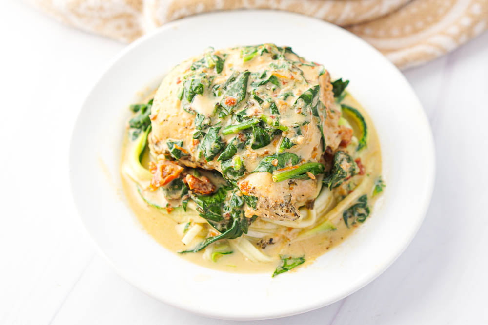 closeup of a white plate with zucchini noodles and creamy chicken and spinach on top