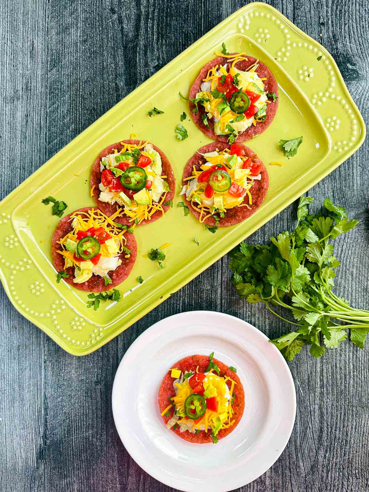 Low Carb Salami Tostadas - only 5 minutes to make and 0.6g net carbs per serving! A tasty, low carb appetizer too! Aerial view of the green platter and white plate with the 5 minute keto salami tostada bites.