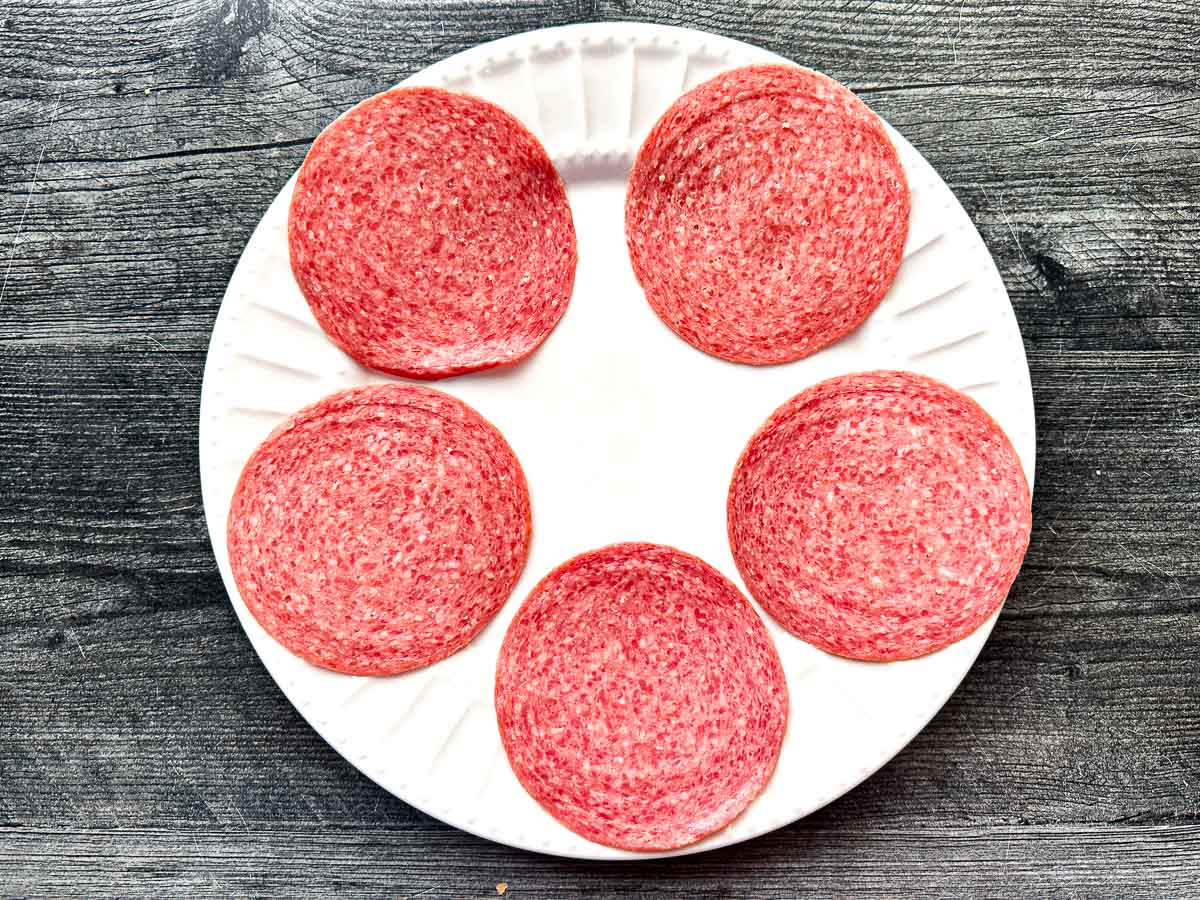 Low Carb Salami Tostadas - only 5 minutes to make and 0.6g net carbs per serving! A tasty, low carb appetizer too! White plate with 5 slices of salami.
