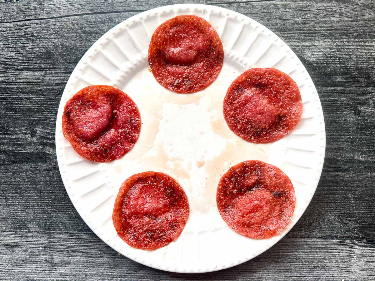 White plate with 5 cooked pieces of salami.