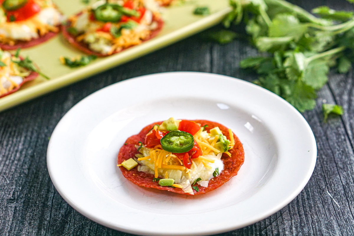 Low Carb Salami Tostadas - only 5 minutes to make and 0.6g net carbs per serving! A tasty, low carb appetizer too! Closeup of a white plate with one of the finished low carb salami snacks.