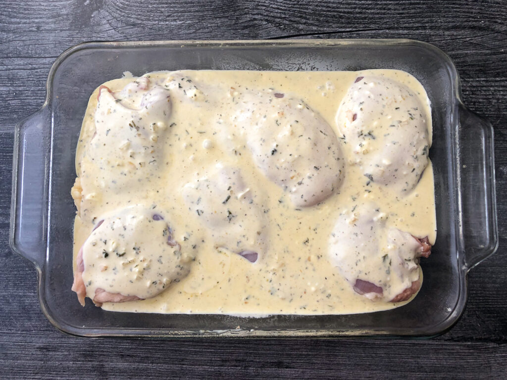 baking dish with raw chicken covered in creamy parmesan sauce