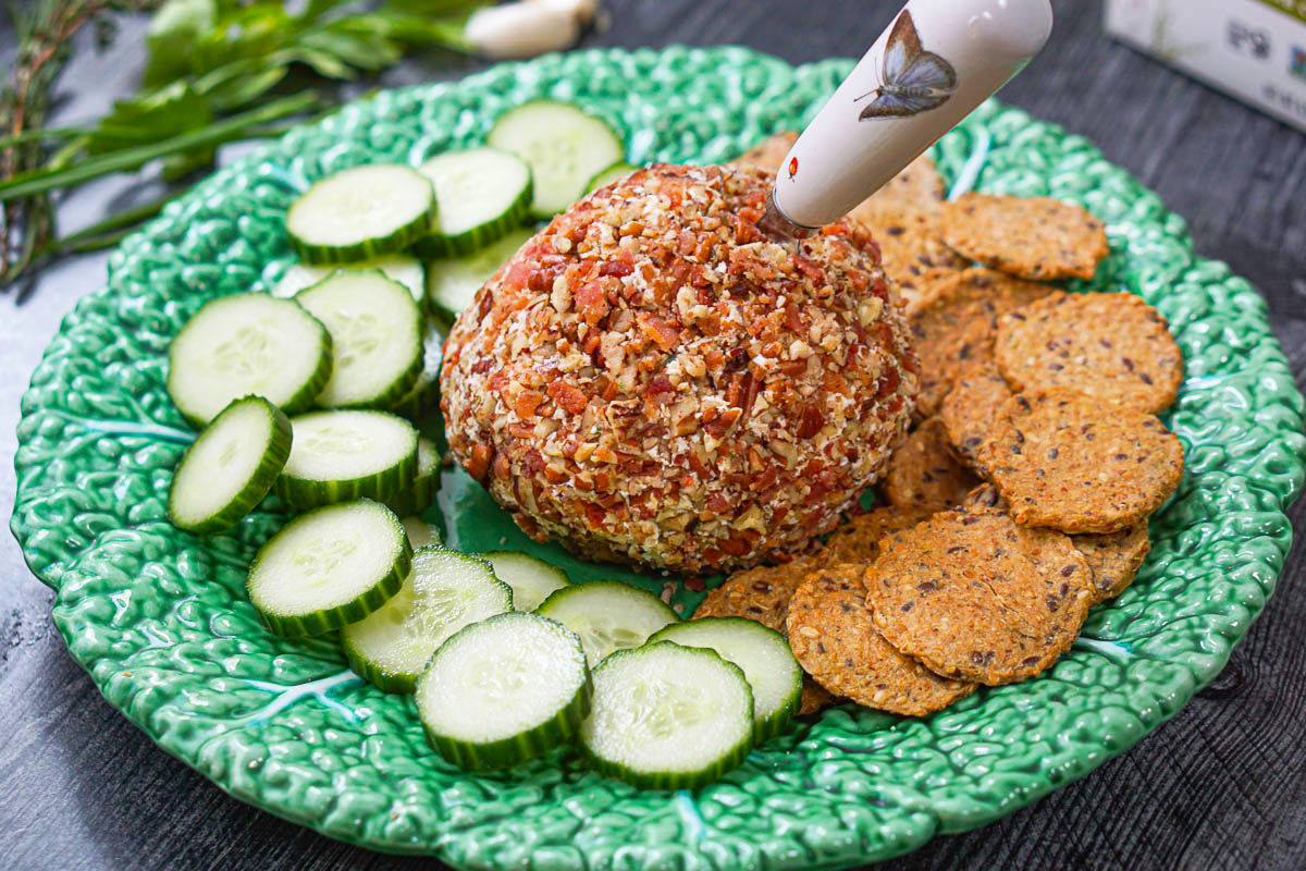 green plate with keto bacon and herb oat cheese ball with cucumbers and crackers