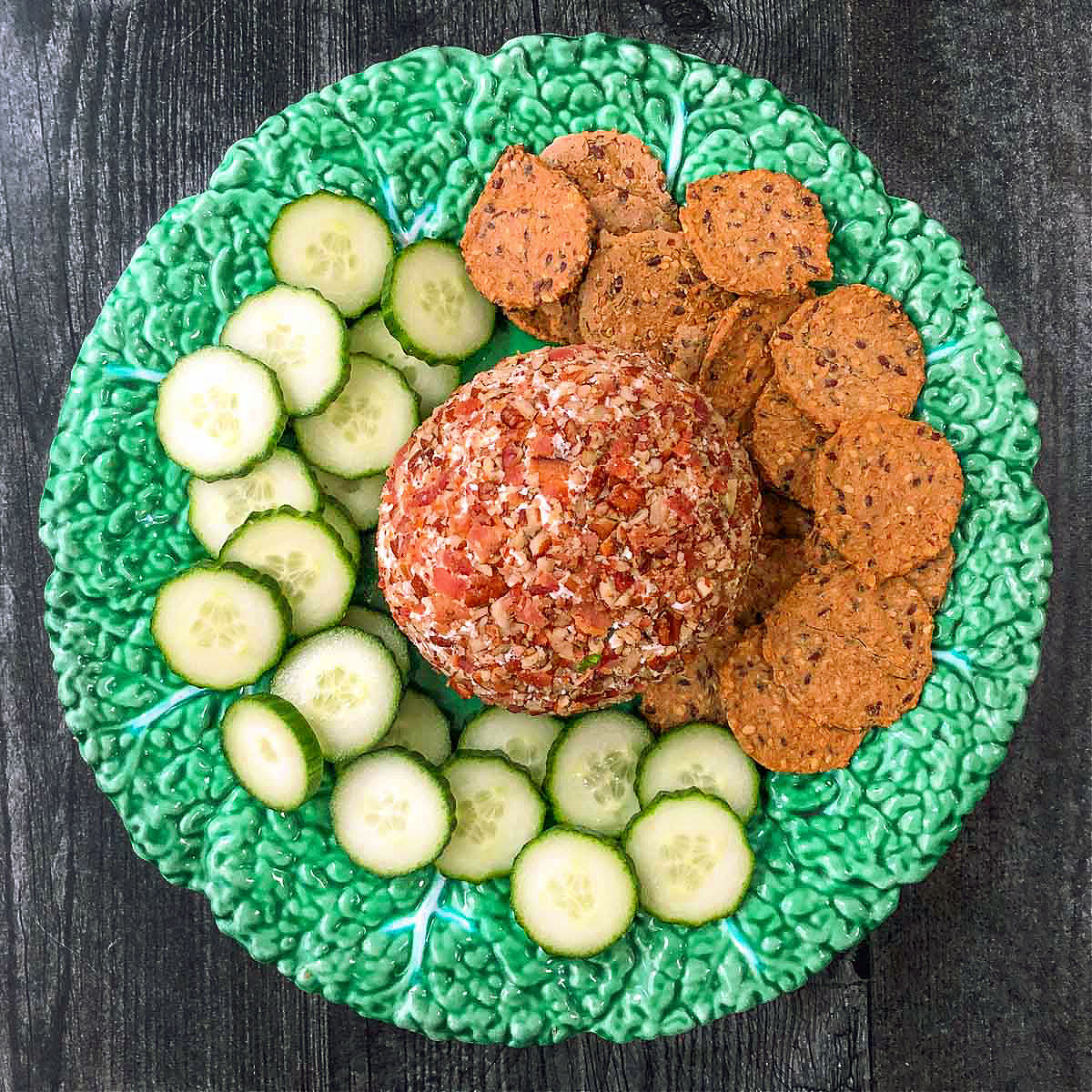 green plate with keto goat cheese ball with cucumbers and crackers