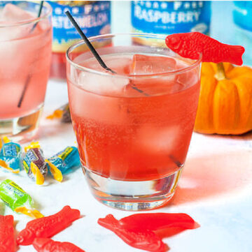 a glass of keto Swedish fish cocktail with scattered candy Swedish fish and bottles in the background