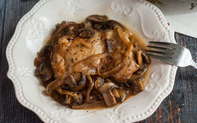 a white plate with a serving of chicken with balsamic onions and mushrooms and a fork