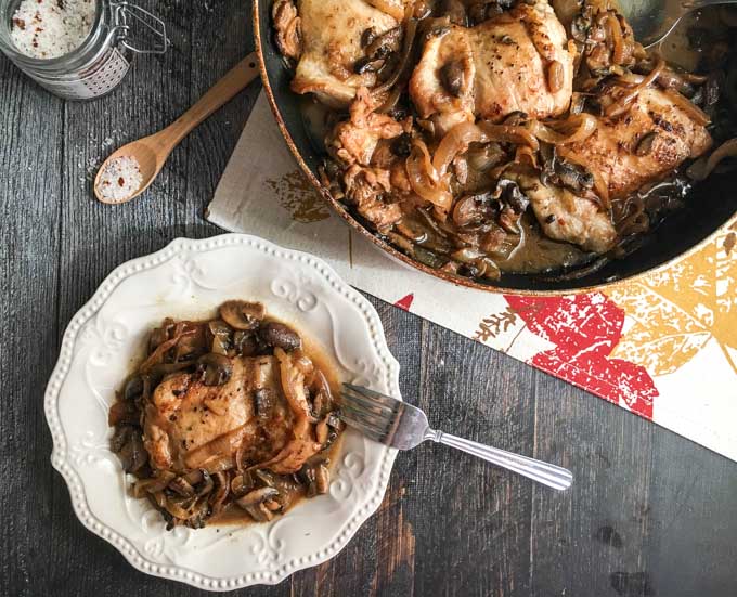aerial view of a white plate with a serving of chicken with balsamic onions and mushrooms and a skillet 