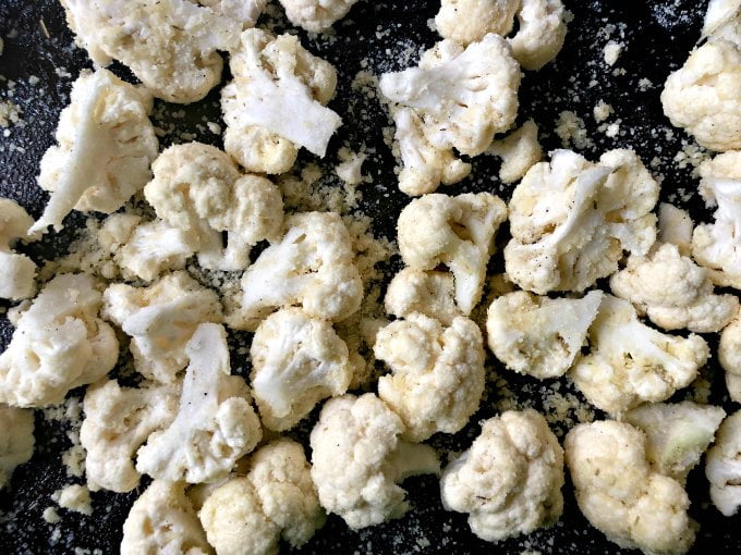raw cauliflower florets coated in parmesan on a cookie sheet
