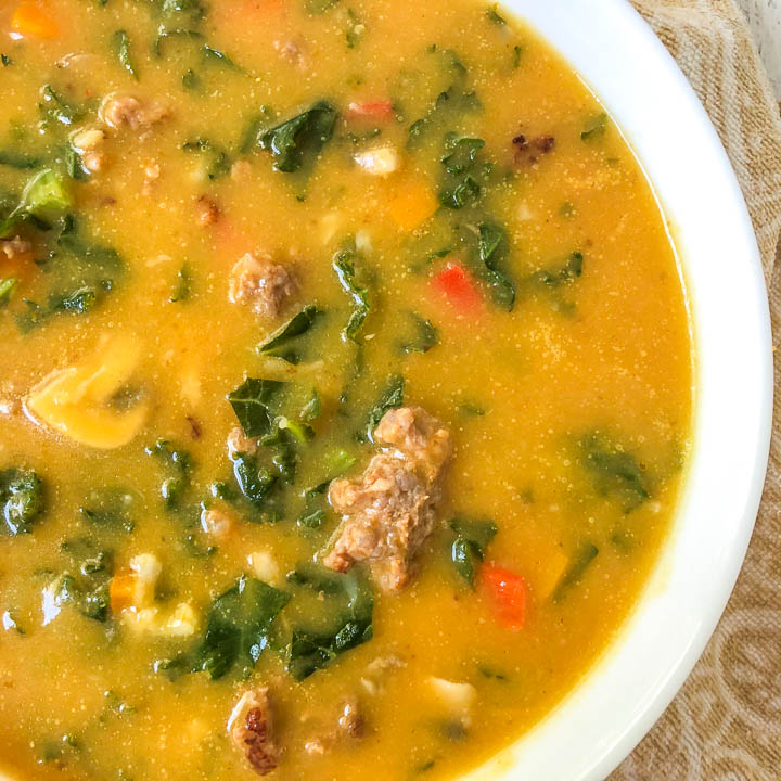 closeup of white bowl with creamy keto pumpkin soup with sausage and kale