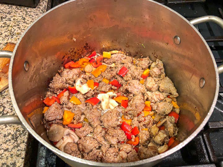 soup pan on the stove with sausage, peppers and mushrooms browning