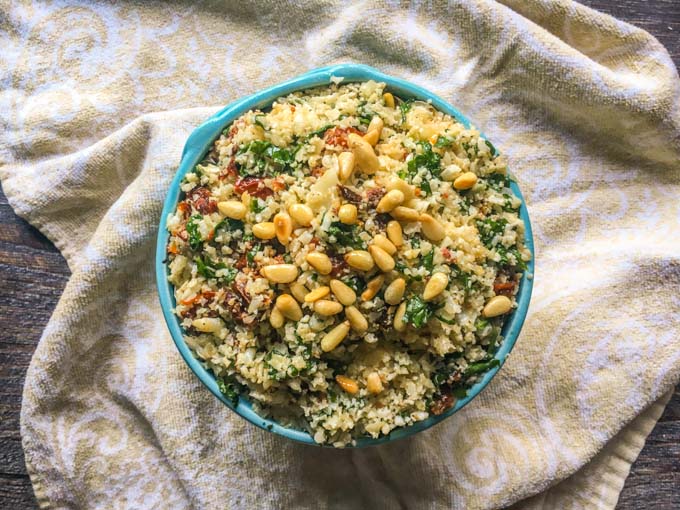 This festive tomato and spinach cauliflower rice only takes 15 minutes to make and is a delicious low carb side dish. Cauliflower rice takes on the flavors sun dried tomatoes and garlic and is topped with crunchy pine nuts.  #cauliflowerrice #lowcarbsidedish #cauliflower #lowcarb