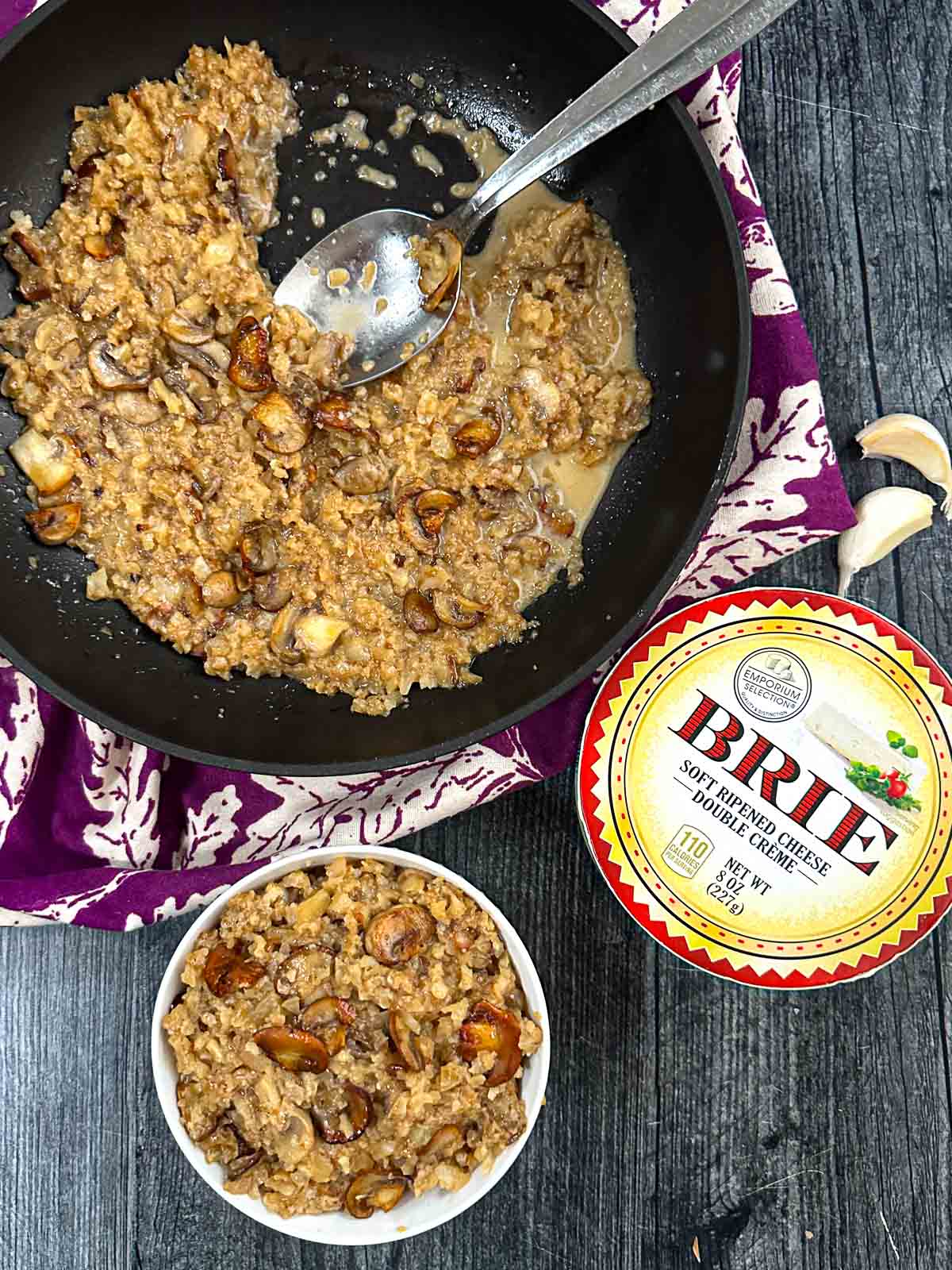 Aerial view of a pan and bowl of keto mushroom cauliflower risotto and box of brie nearby.