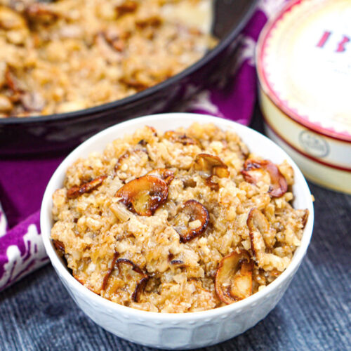 White bowl with keto mushroom cauliflower risotto and a box of brie in the background and fresh mushrooms on the side.