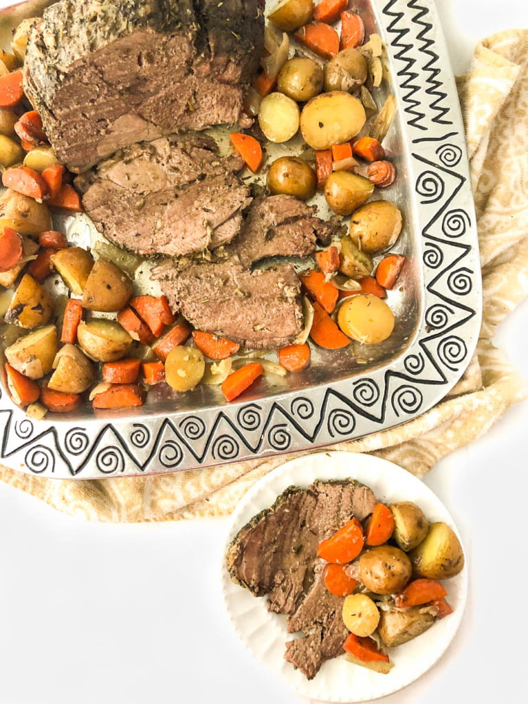 aerial view of a metal platter with a lamb roast and scattered roasted potatoes and carrots