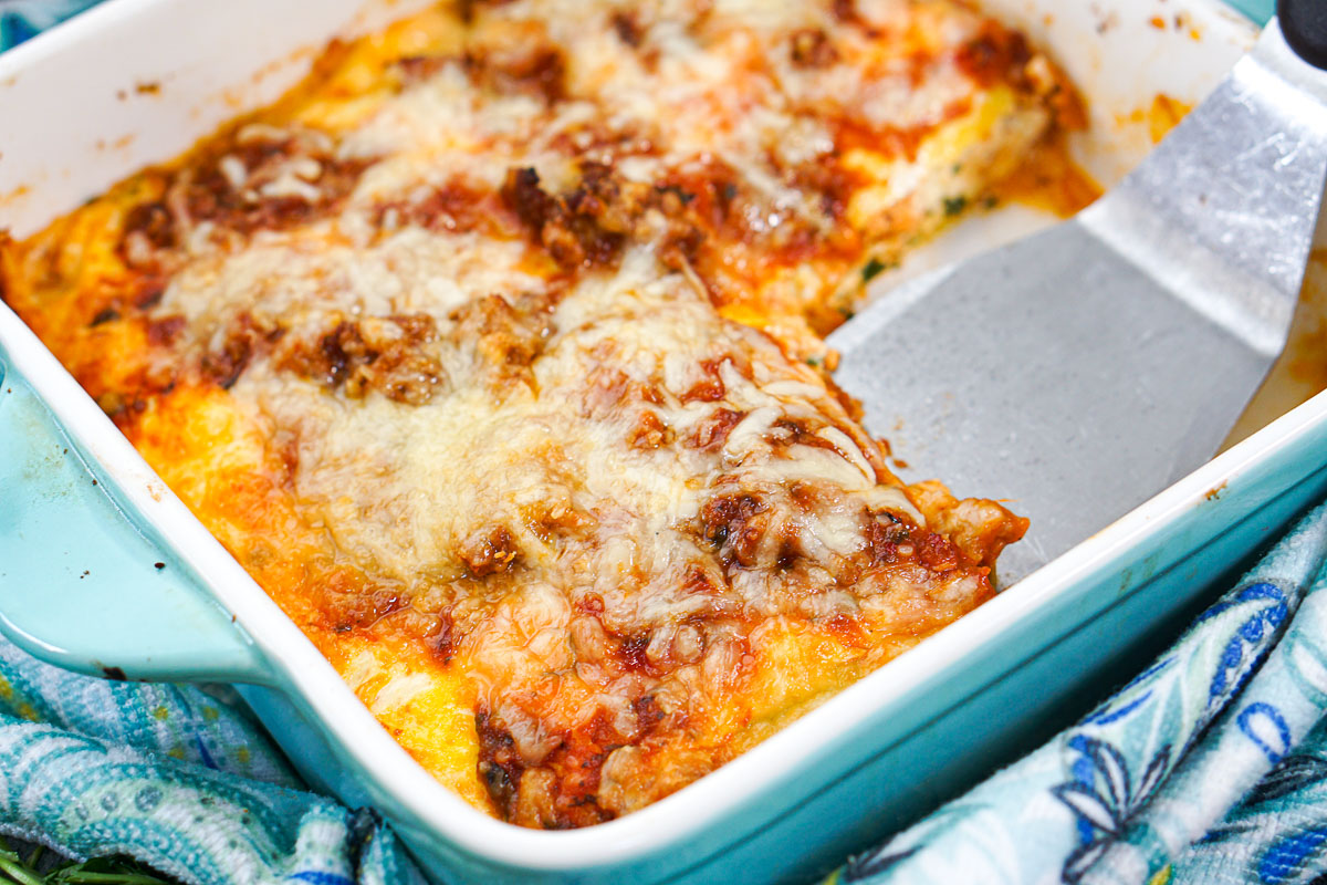 lasagna in baking dish with a piece missing and a silver spatula