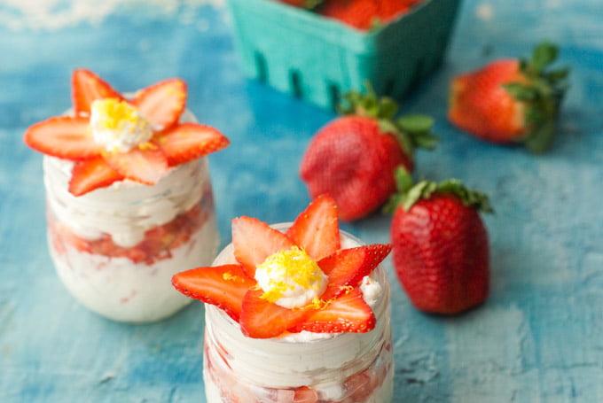 closeup of no bake cheesecake jars and raw strawberries on blue table
