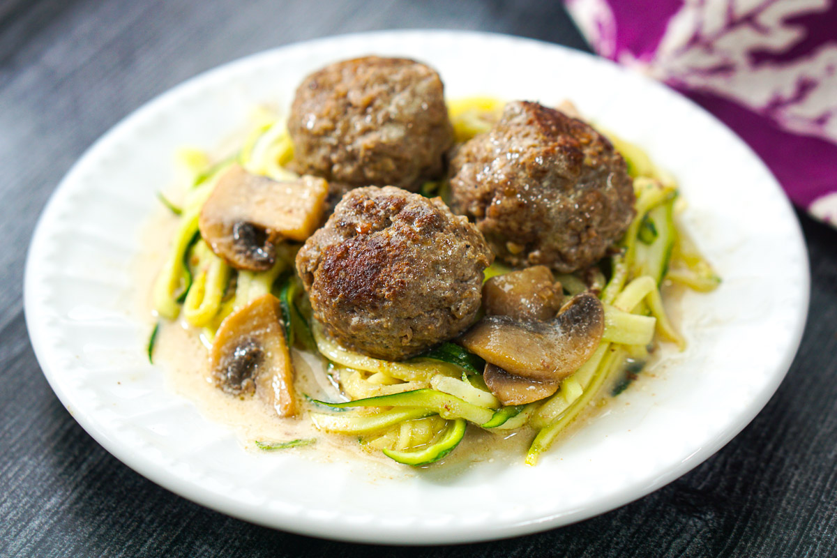 closeup of a white plate with zucchini noodles and meatballs
