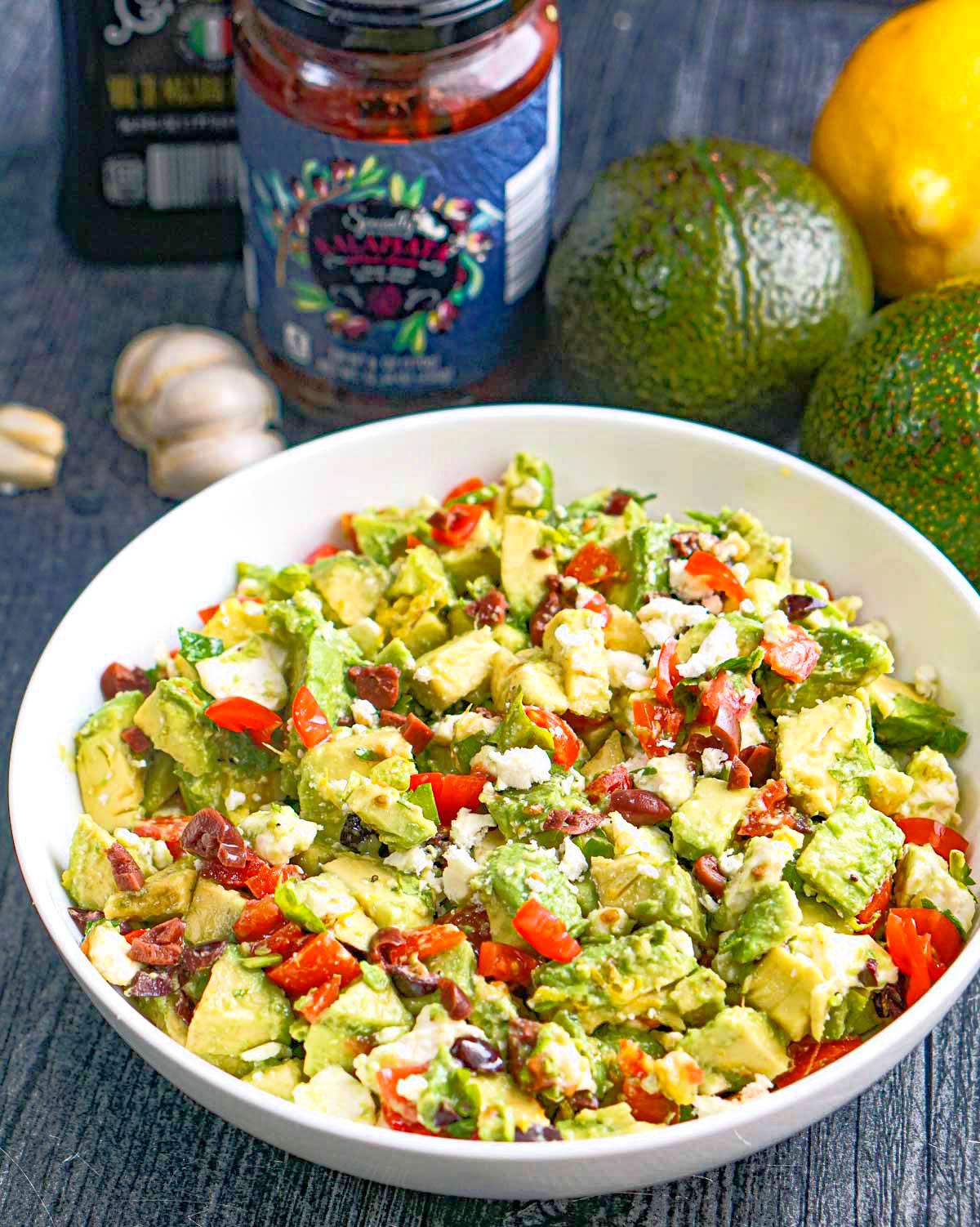 Closeup of a bowl of Greek chunky guacamole dip and ingredients in the background.