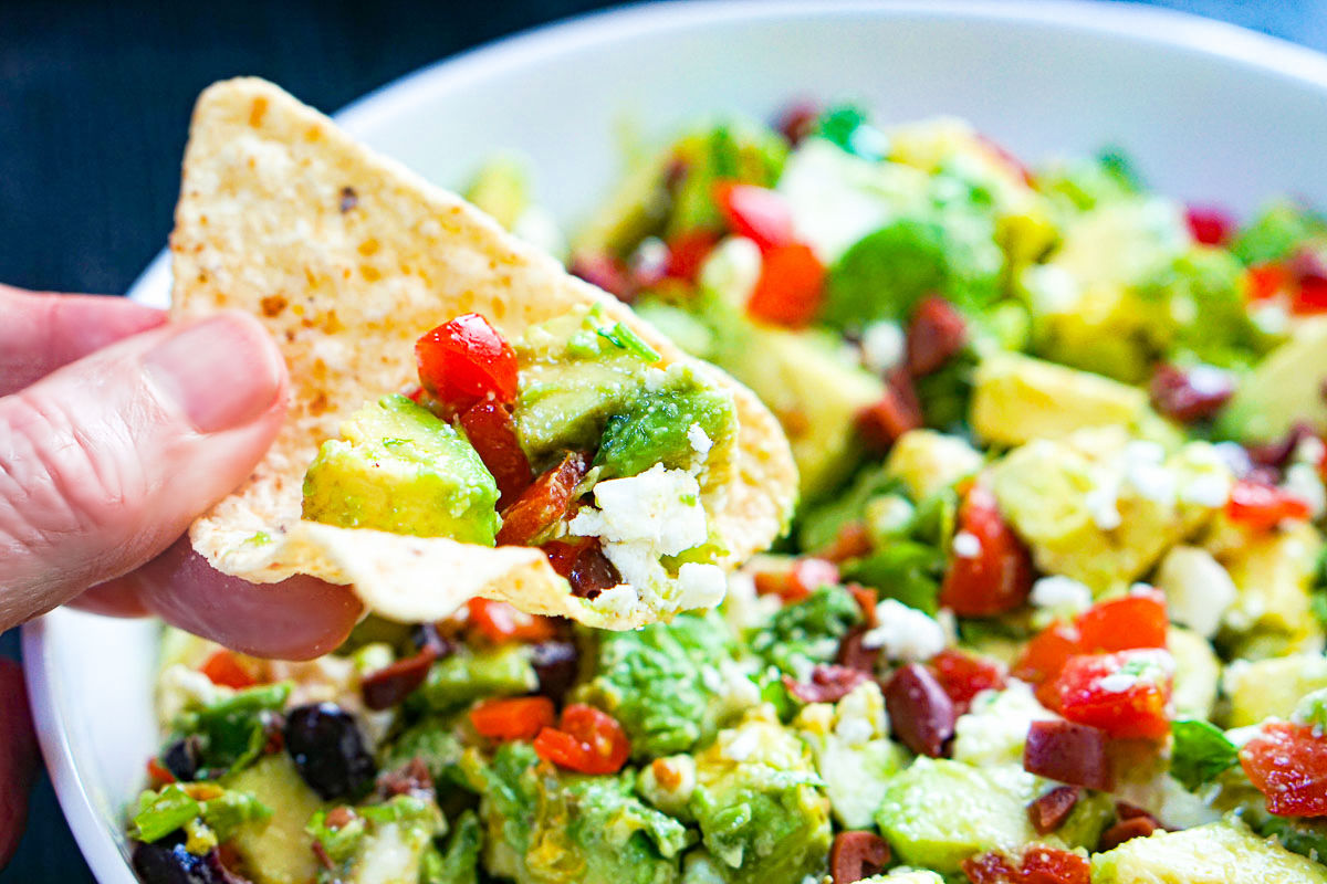 A hand holding a tortilla chip with the finished guacamole.