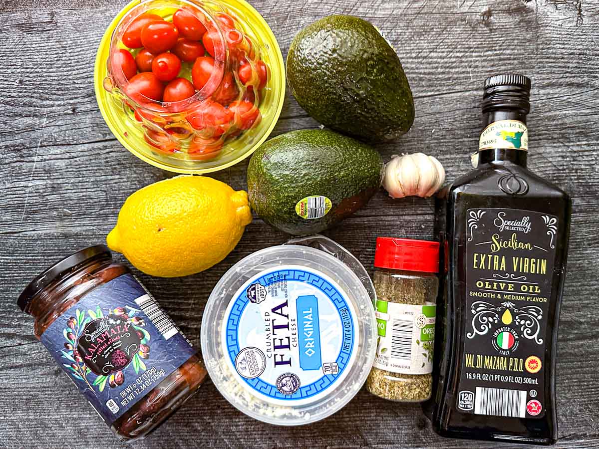 Recipe ingredients - grape tomatoes, avocados, lemons, garlic, oregano, feta cheese, olives and olive oil.