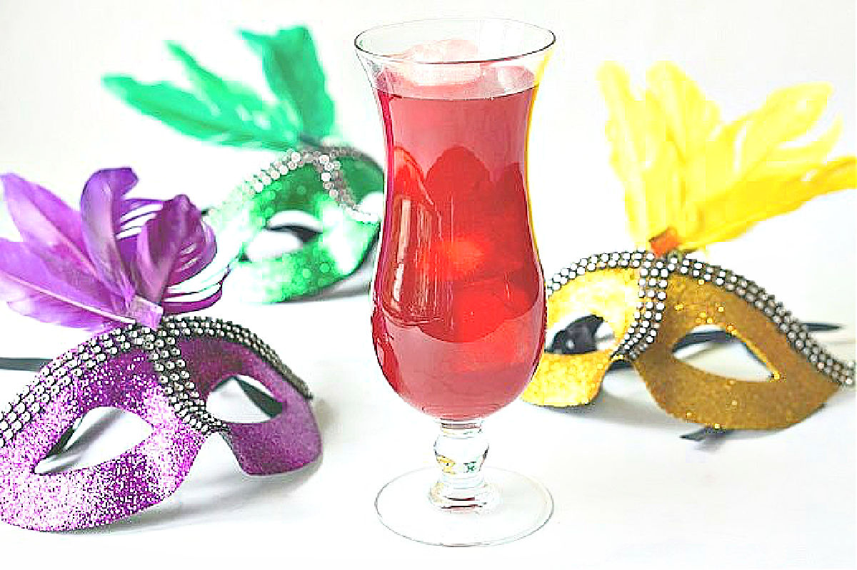 A glass of the hurricane drink with a purple, gold and green mask.