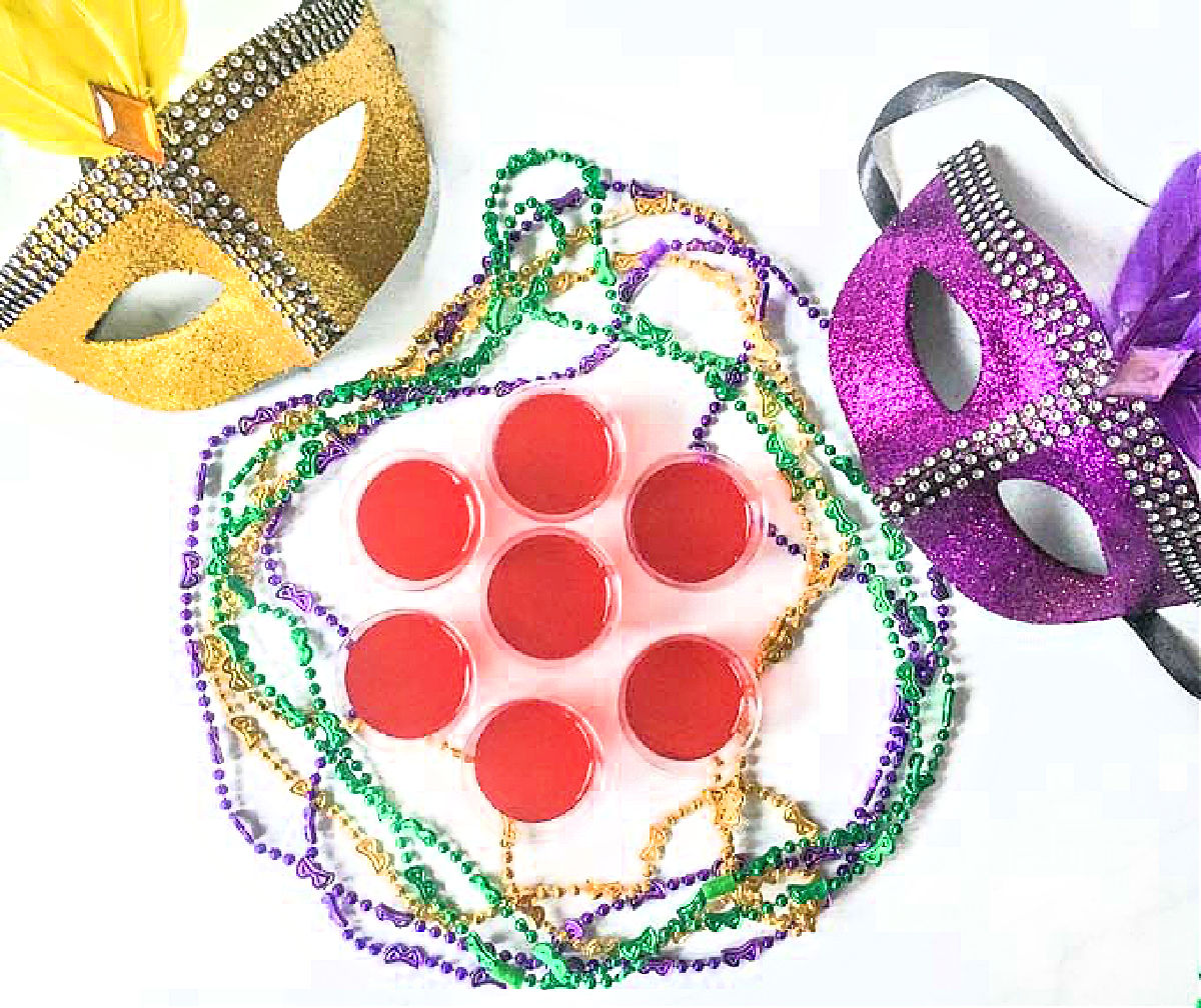 Aerial view of a bunch of jello shots surrounded by Mardi Gras beads and masks.