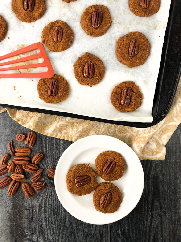 aerial view of a cookie sheet and white plate with healthy pecan pumpkin cookies and scattered pecans