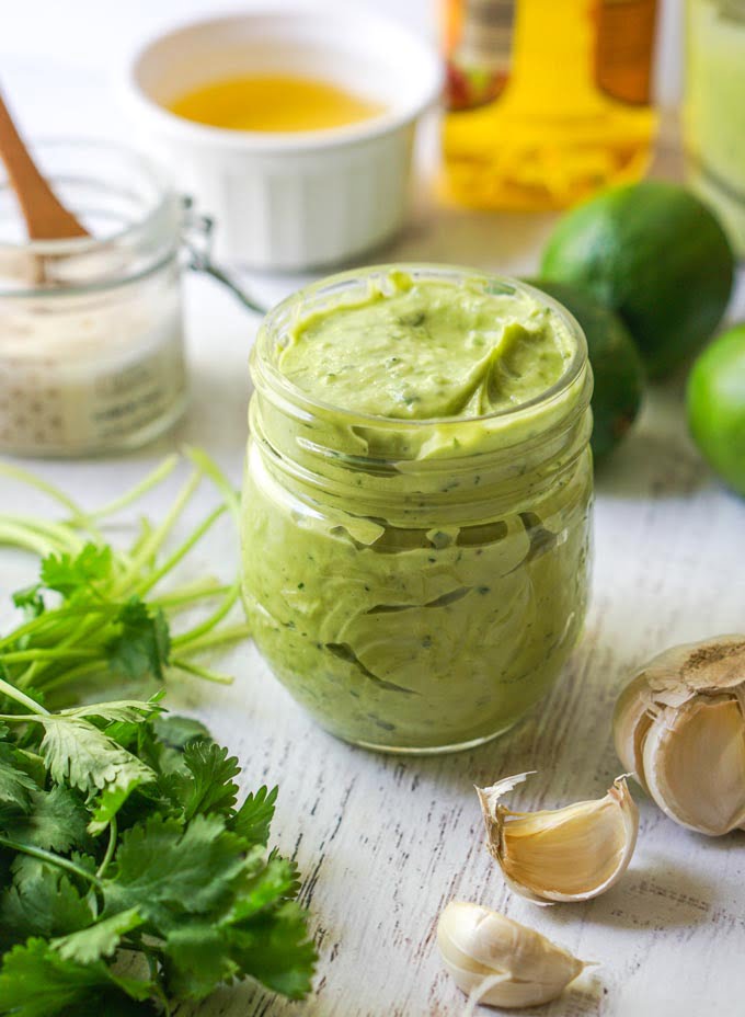 jar with creamy avocado lime dressing and cloves of garlic, fresh cilantro and limes scattered