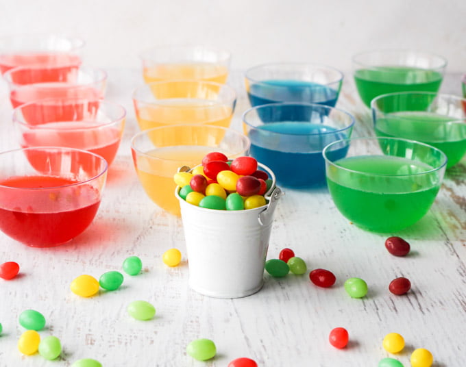 rainbow colored gelatin dishes with a little bucket full of jelly beans in front