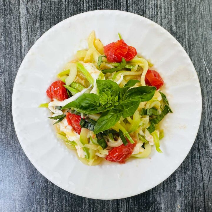 Aerial view of white plate with zucchini caprese pasta.