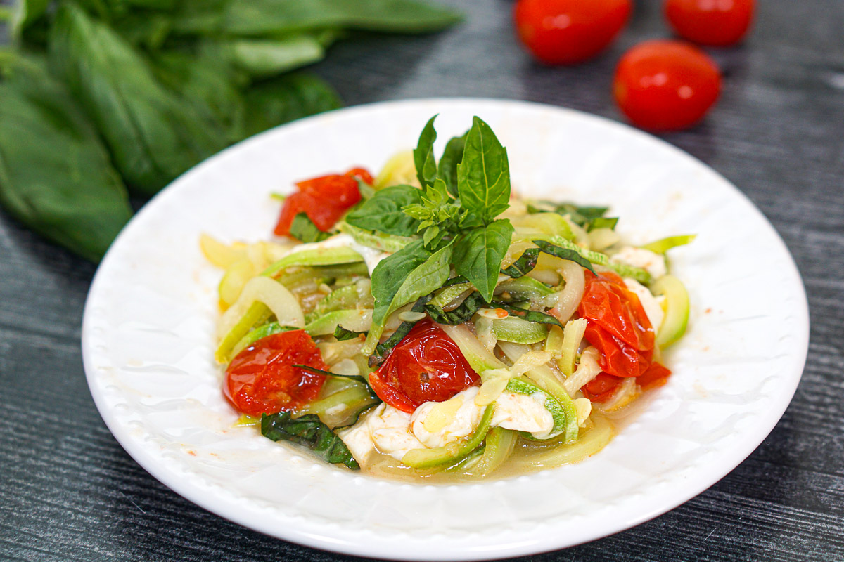Closeup of a white plate with a serving of the zucchini noodles with fresh mozzarella and basil.