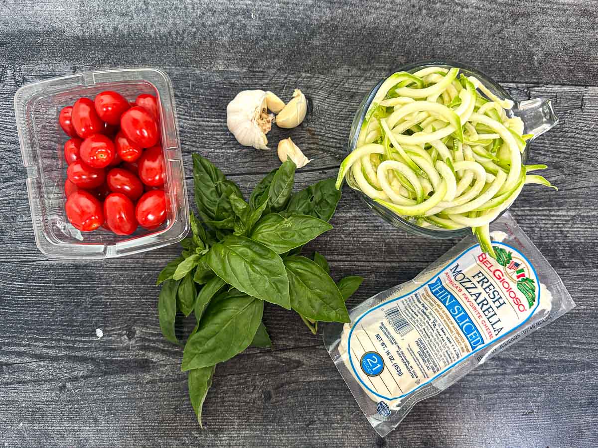 Recipe ingredients - fresh garlic, zucchini noodles, fresh basil leaves, tomatoes and fresh mozzarella.