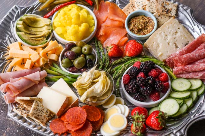  a silver platter with a selection of low carb finger foods such as cheeses, olives, berries, low carb vegetables, etc