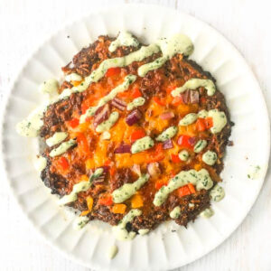 A white plate with a mini Mexican meat crust pizza or meatza with taco toppings.
