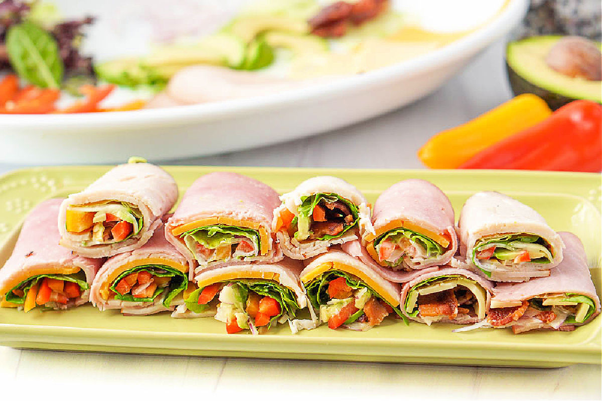 green platter with deli meat rolled up with fresh veggies and cheese