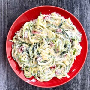 Aerial view of a red plate with keto creamy sun dried tomato sauce covered zucchini noodles.