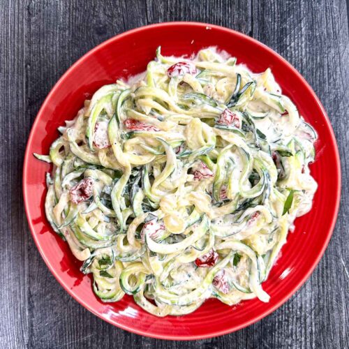 Aerial view of a red plate with keto creamy sun dried tomato sauce covered zucchini noodles.