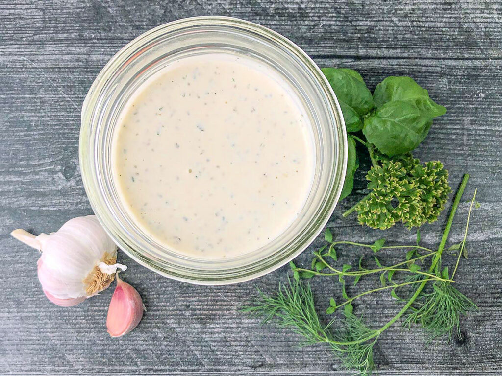 aerial view of a jar of ranch, garlic cloves and fresh herbs