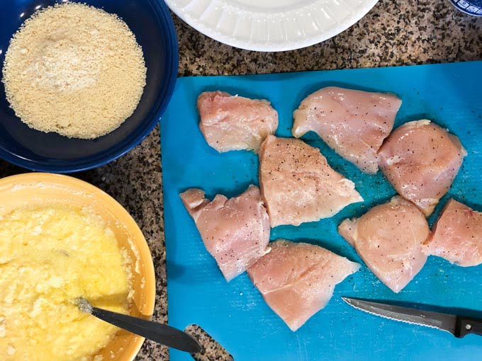 raw chicken on cutting board with almond flour and egg mixture 