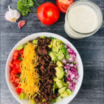 aerial view of keto taco salad with keto ranch dressing and fresh tomatoes, garlic and herbs and text