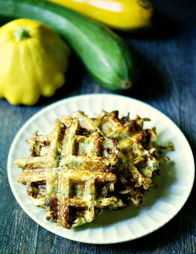 savory low carb zucchini waffles on a white plate with squash and zucchini in the background
