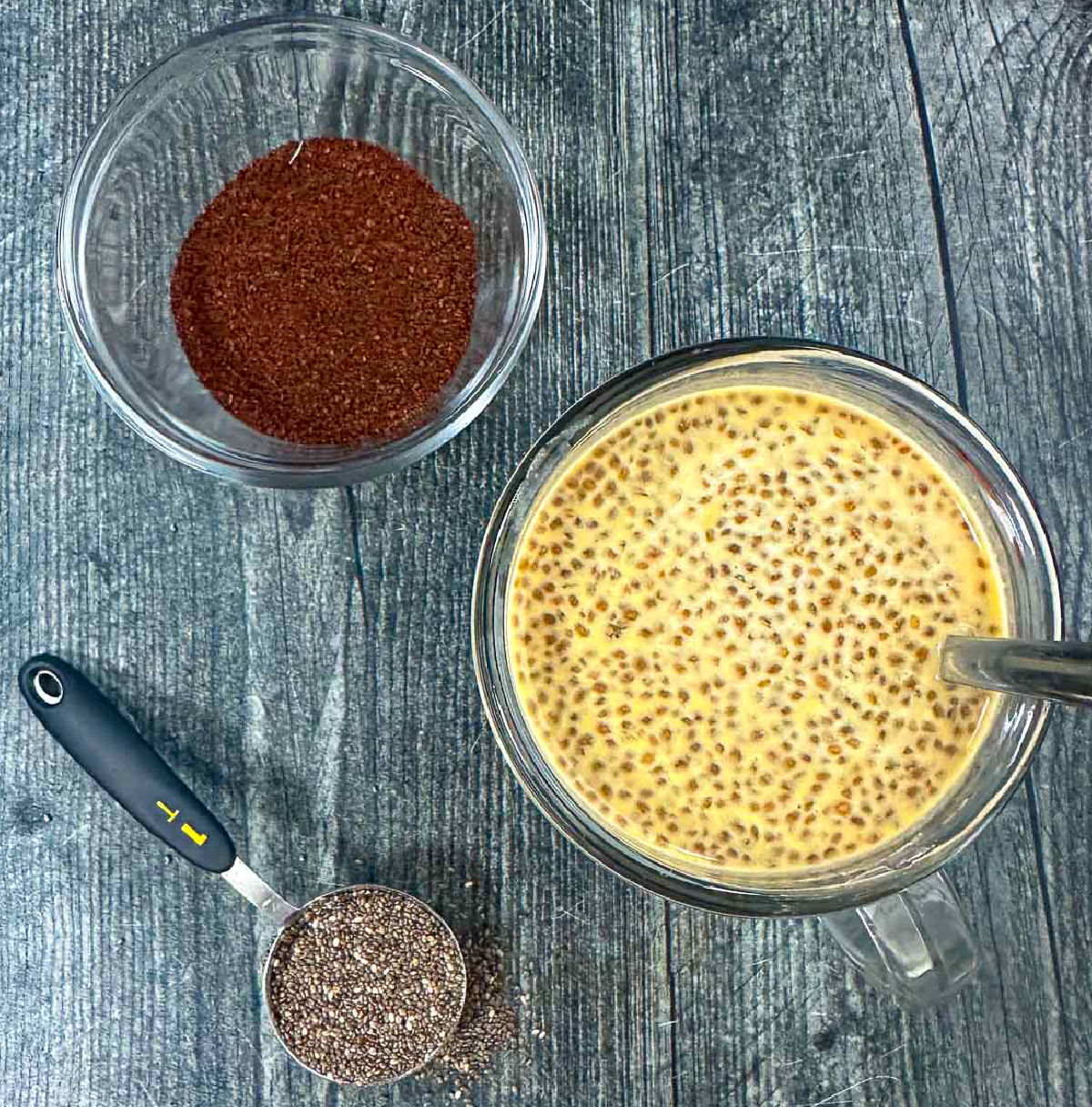 Aerial view of a mug of chia protein pudding and a spoonful of chia seeds and some coffee.